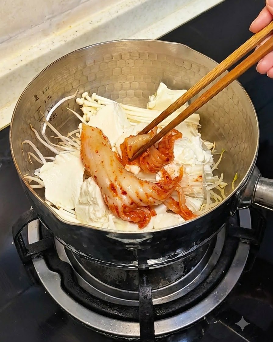 Stäbchen legen Stücke von rotem, fermentiertem Kimchi über den Tofu, die Pilze und die Sprossen in den Topf.