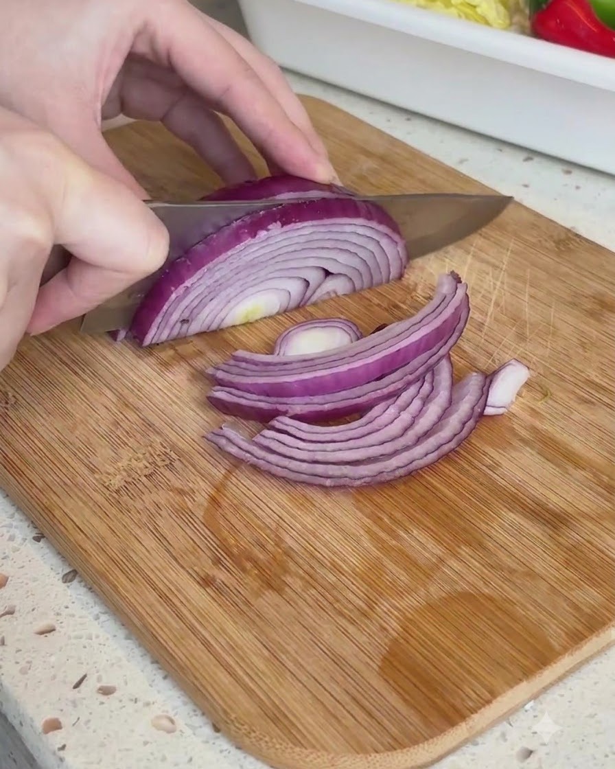 Die Hälfte einer roten Zwiebel wird auf einem Holzschneidebrett in dünne Streifen geschnitten.