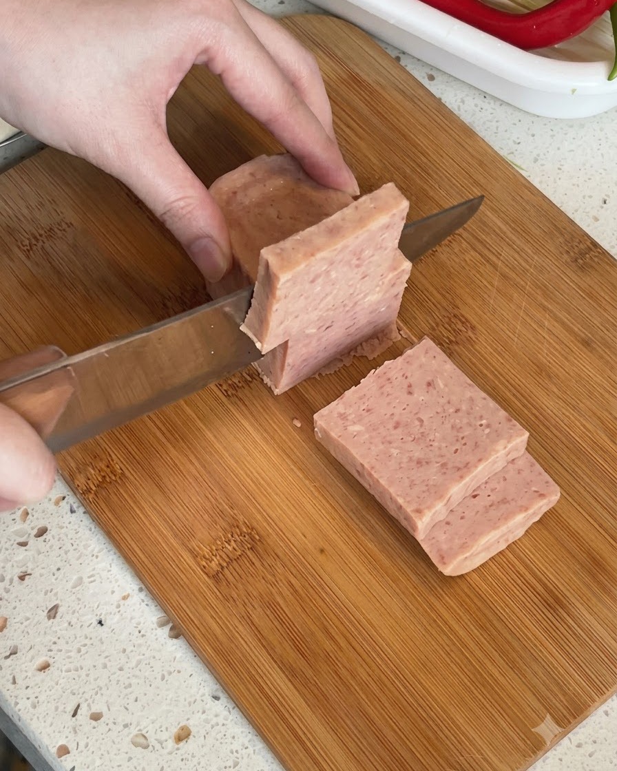 Ein Block Dosenfleisch wird auf einem Schneidebrett in dicke Scheiben geschnitten.