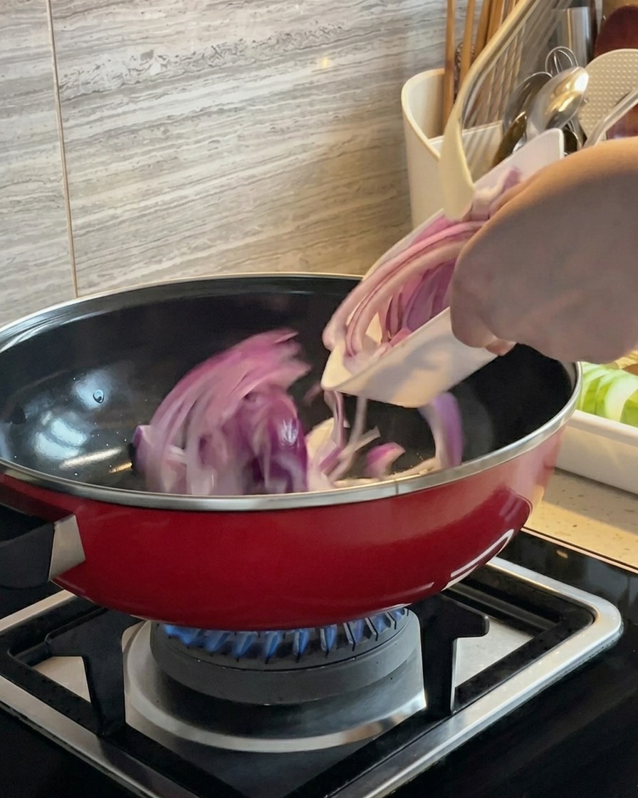 Rote Zwiebelscheiben werden in einem roten Topf über einem Gasbrenner geschwenkt und angebraten.