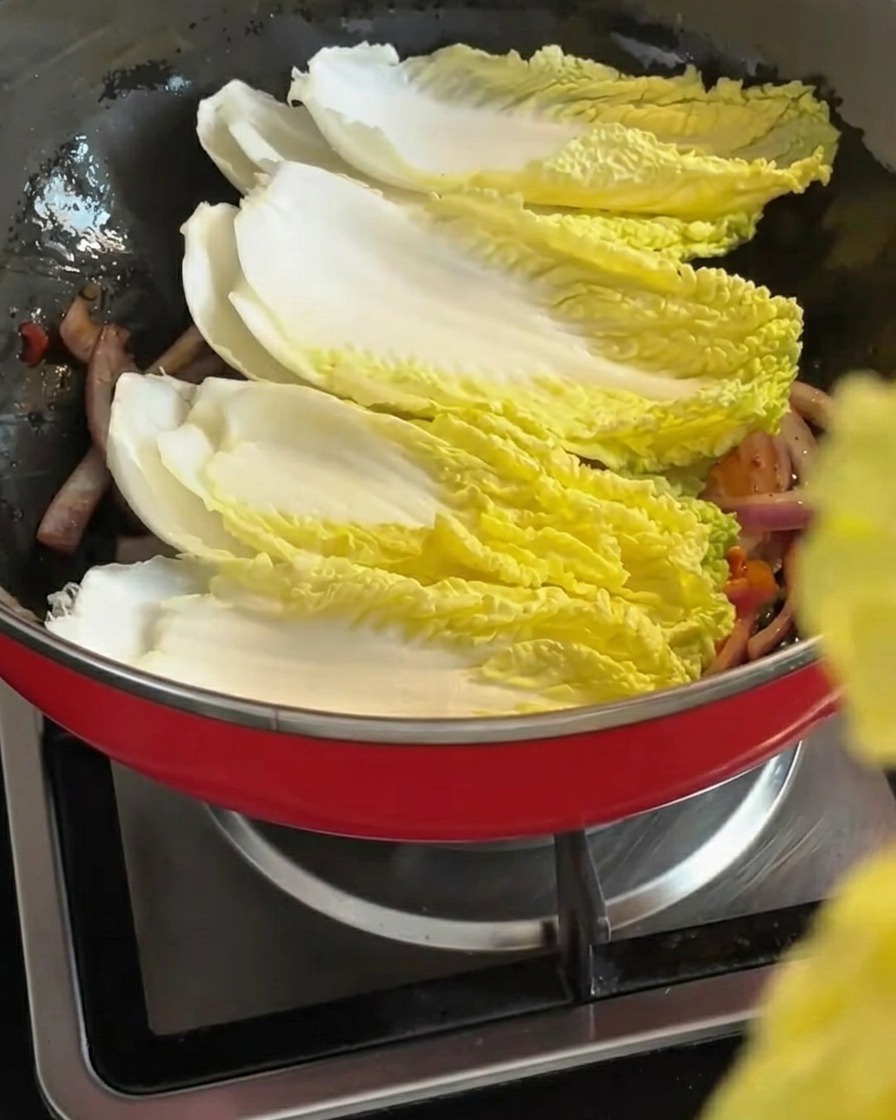 Frische Napfkohlblätter werden über die angebratene Zwiebel-Kimchi-Mischung geschichtet.