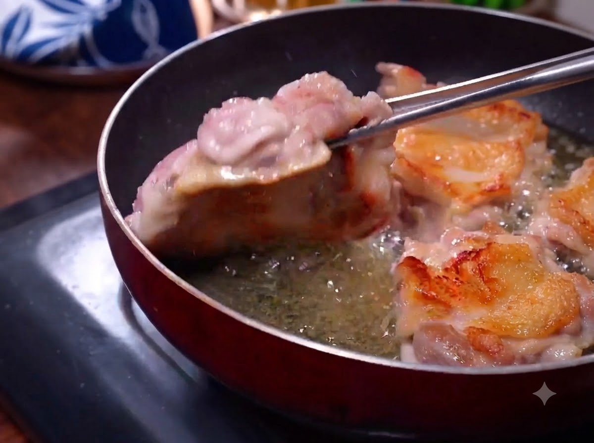 Hähnchenschenkel braten in einer Pfanne, die goldbraune Haut ist sichtbar, während eine Zange sie wendet.