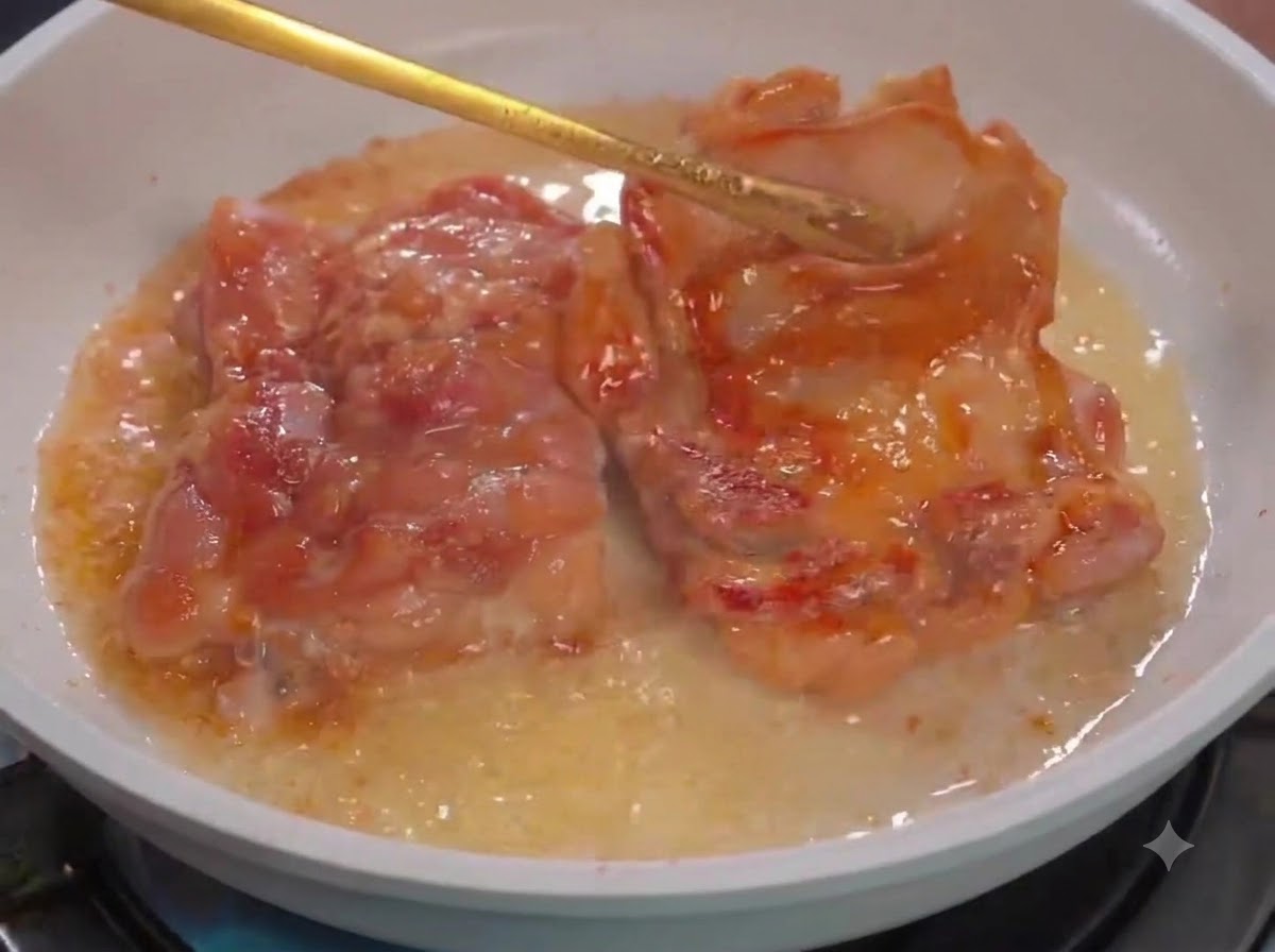 Eine Küchenzange wendet Hähnchenstücke in einer weißen Pfanne mit Öl.