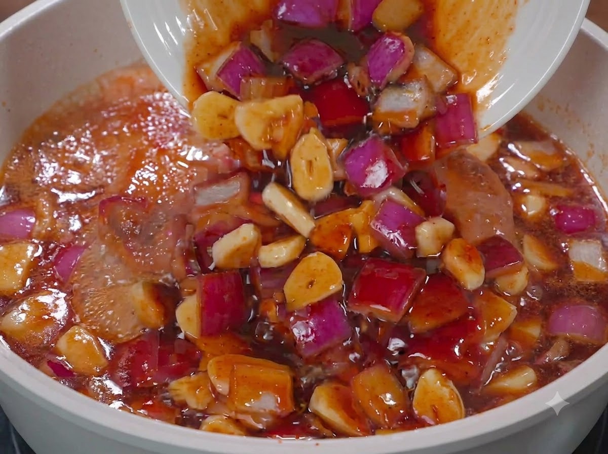 Sauce und rote Zwiebeln werden von einem weißen Teller in eine Pfanne mit Hähnchen gegossen.