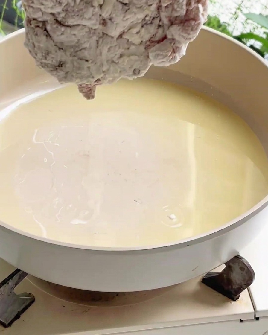 Ein mit Stärke umhülltes Hähnchenstück wird in eine breite Pfanne mit heißem Speiseöl auf dem Herd gelegt.