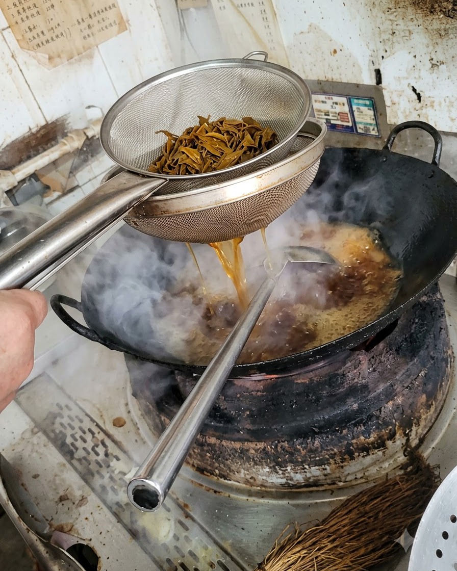 Ein Metall-Seiher mit dunklen, blanchierten Pilzstreifen, während Flüssigkeit in den darunter liegenden Wok tropft.