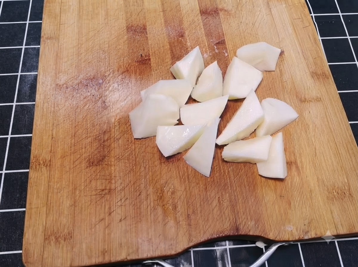 Geschälte Kartoffeln in unregelmäßige, mundgerechte Stücke geschnitten auf einem Holzschneidebrett.