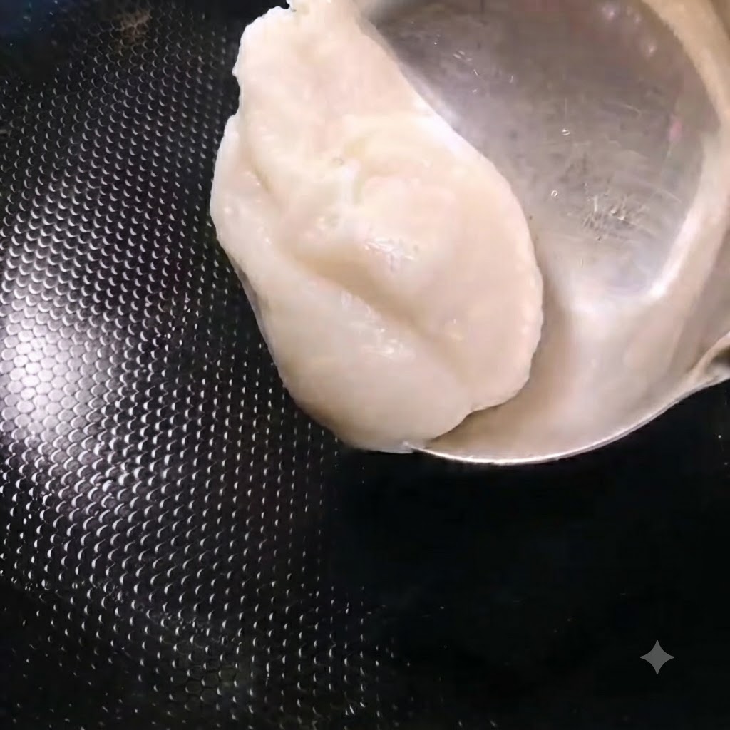 Eine Kelle gibt weißes Schweineschmalz in einen erhitzten schwarzen Wok.