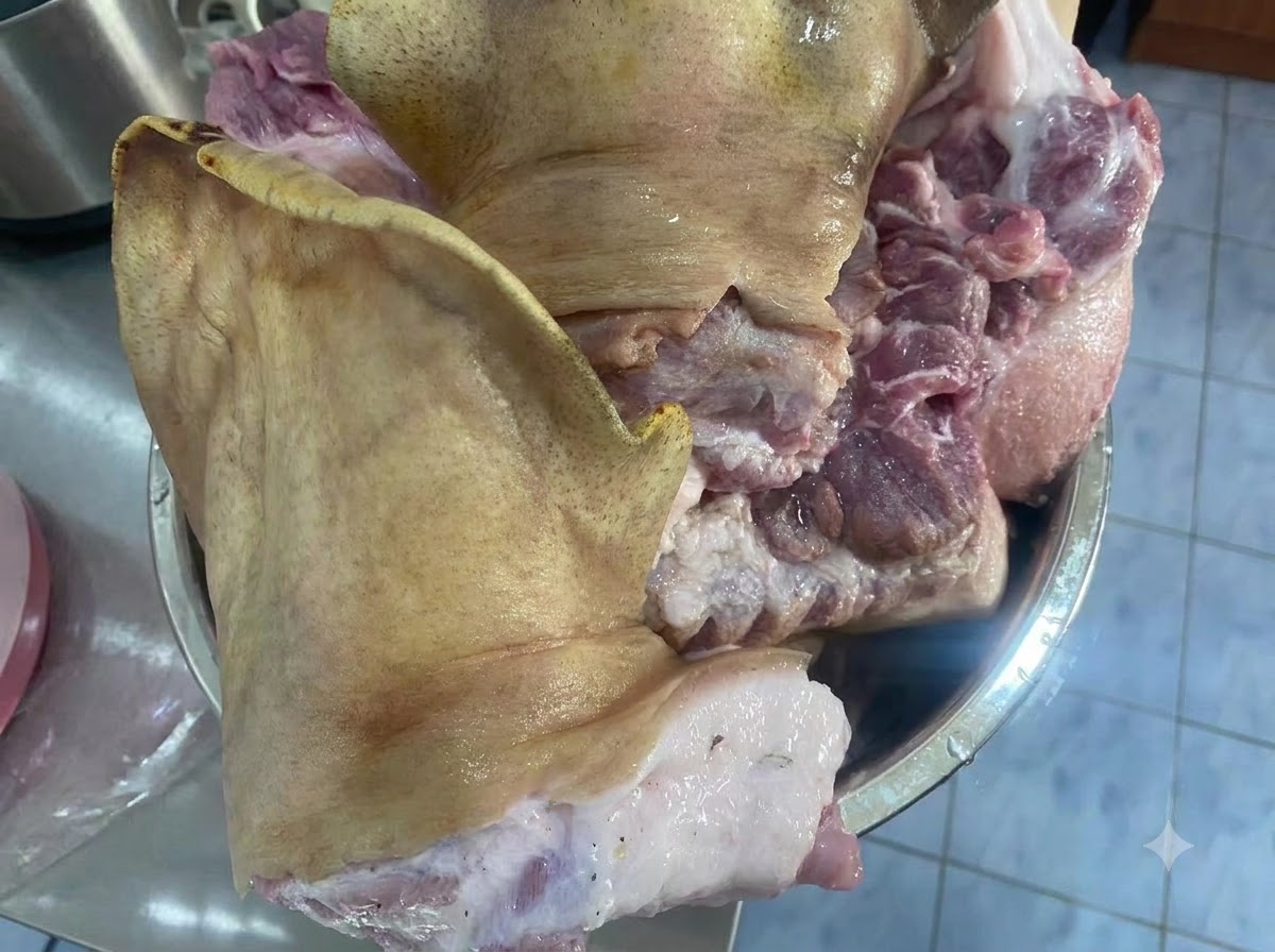 Große rohe Stücke eines Schweinegesichts liegen in einer Metallschüssel auf einer Arbeitsplatte.