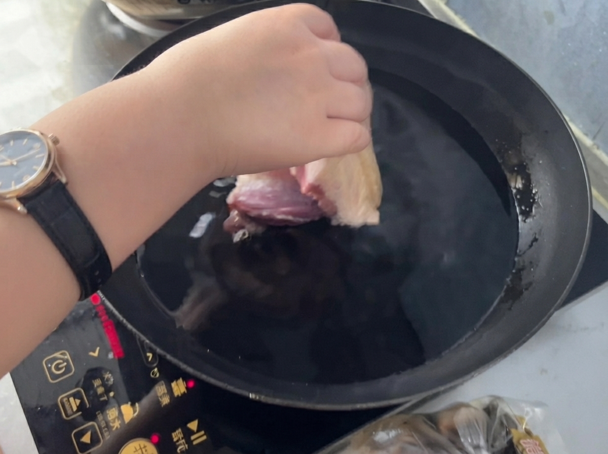 Eine Hand legt ein Fleischstück in einen Topf mit kaltem Wasser, Ingwer und Kochwein.