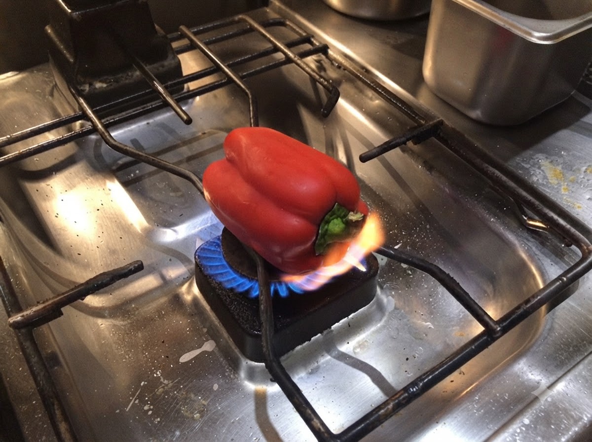 Eine ganze rote Paprika wird direkt über der offenen Flamme des Gasherds geröstet.