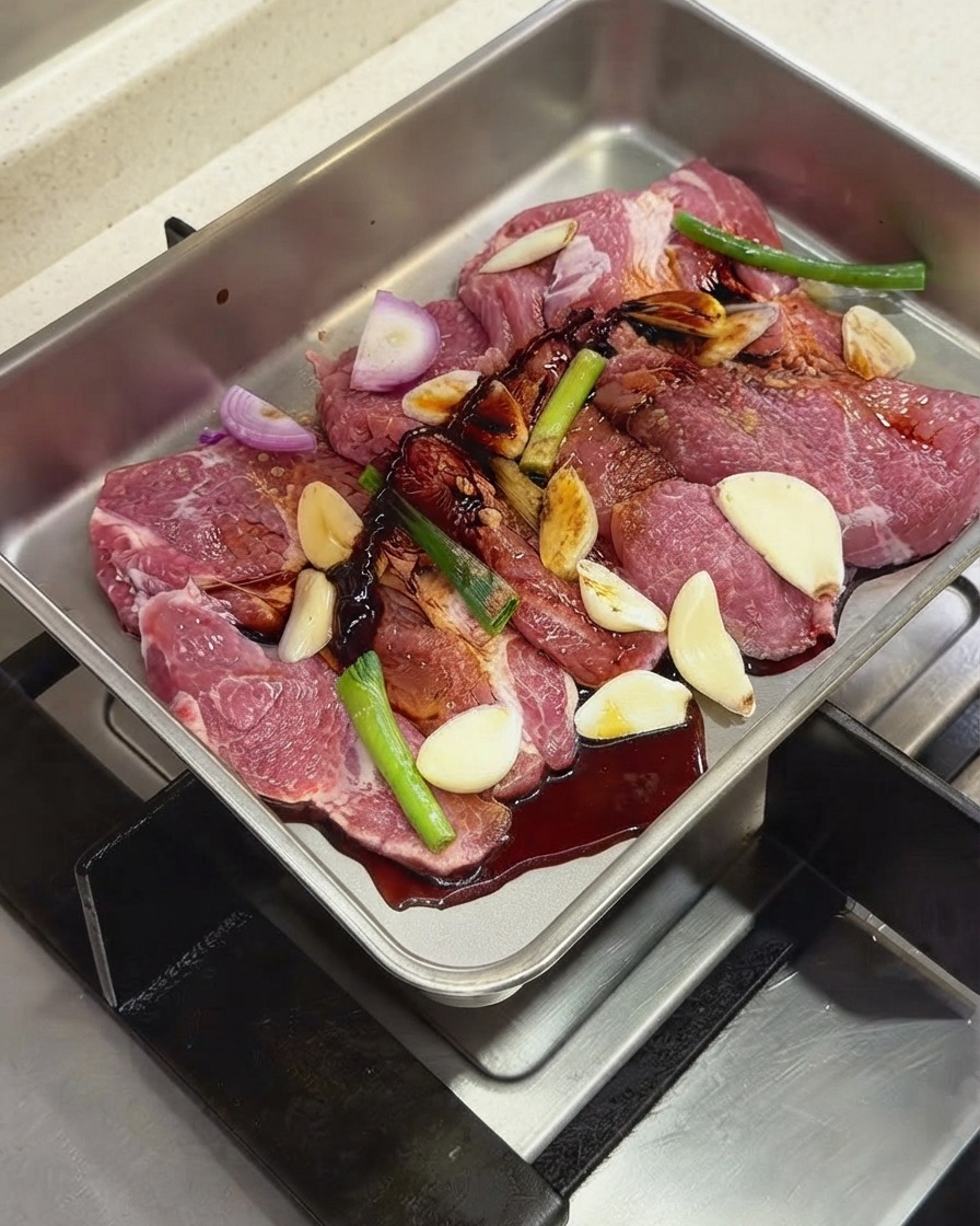 Dunkle Saucen und Gewürze werden über die Schweinekoteletts und Aromen in einer Metallschale gegossen.