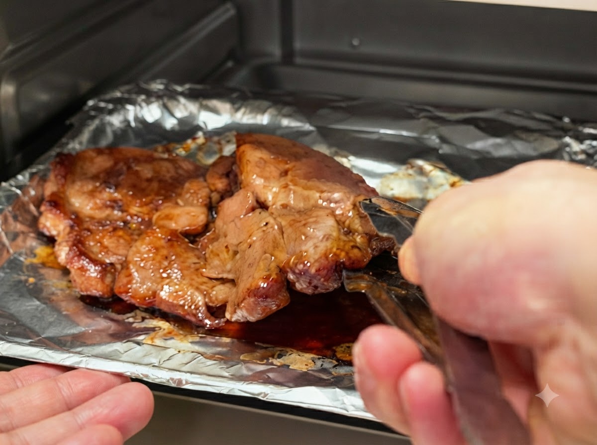 Schweinekoteletts werden mit Küchenzangen aus Metall auf dem Backblech umgedreht.