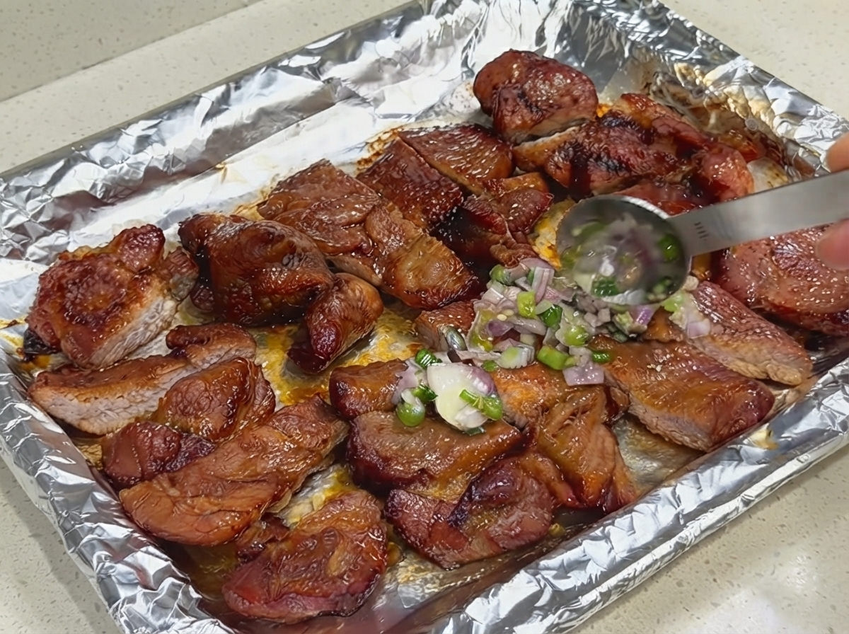 Ein Löffel trägt eine Schicht frischer Frühlingszwiebel- und Schalottensauce auf geschnittenes Schweinefleisch auf einem mit Folie ausgelegten Backblech auf.