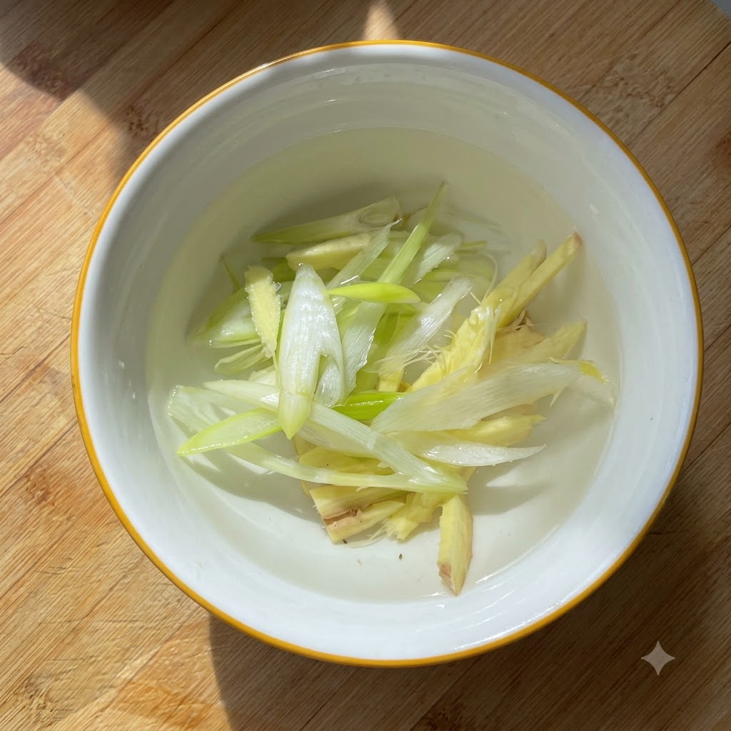In einer kleinen weißen Schüssel mit Wasser eingelegte Frühlingszwiebeln und Ingwerstücke.