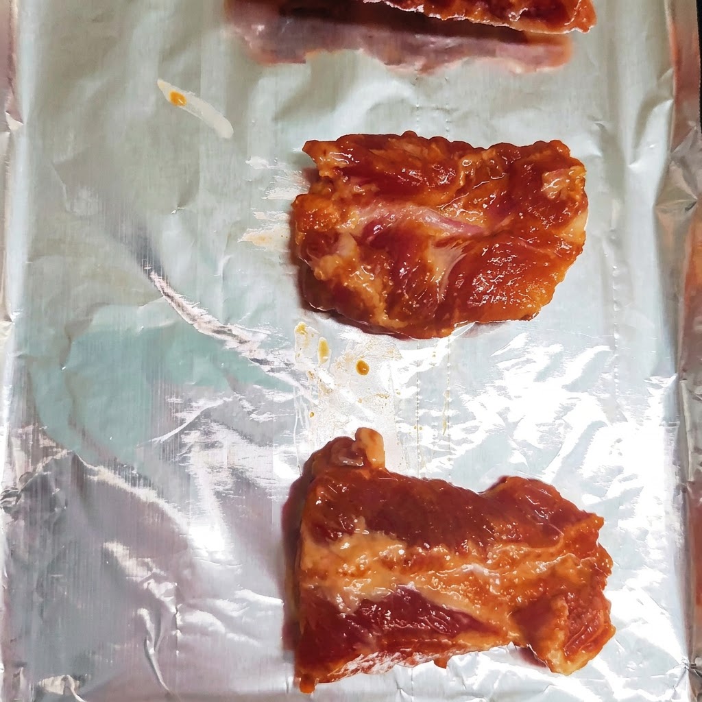 Marinierte Schweinerippchenstücke ordentlich in einer einzigen Reihe auf einem mit Alufolie ausgelegten Backblech platziert.