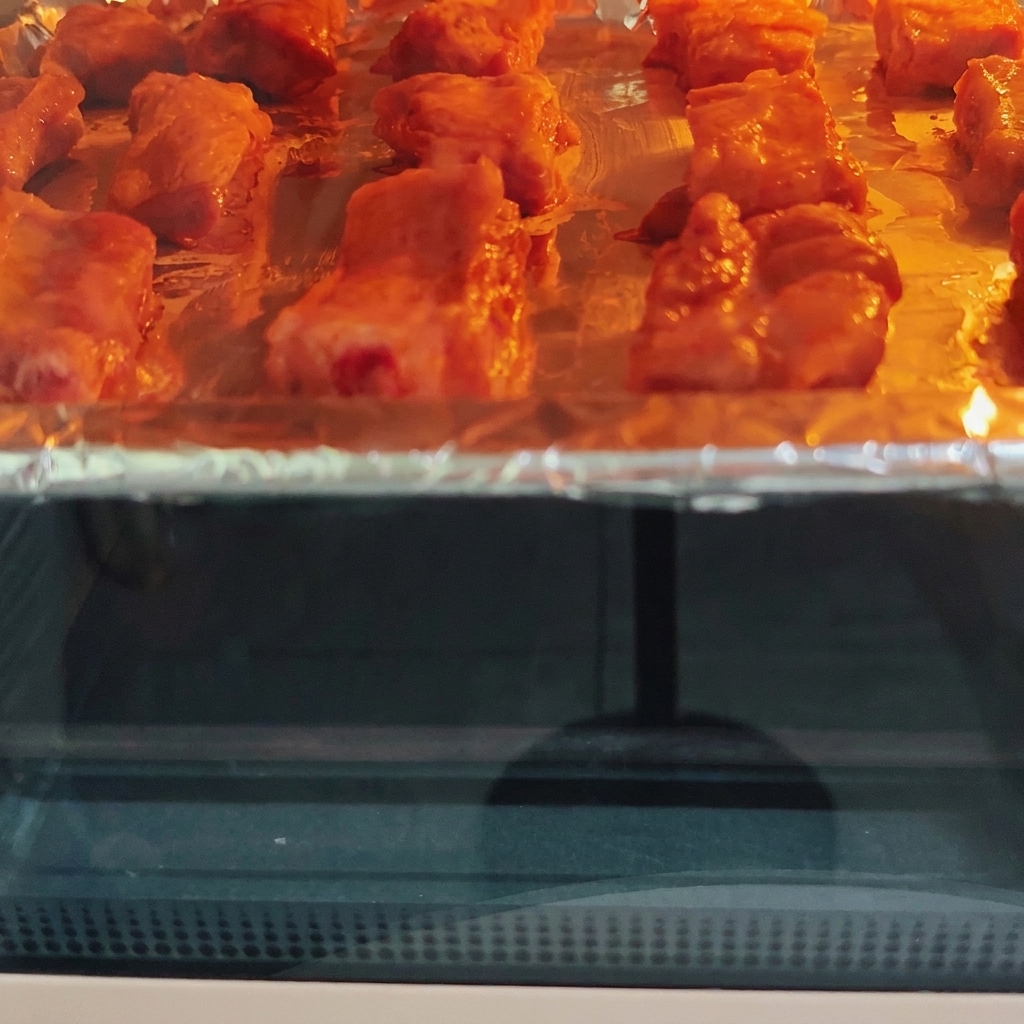 Schweinerippchen garen in einem heißen Ofen auf einem Blech und zeigen sichtbare Bräunung unter dem Heizelement.