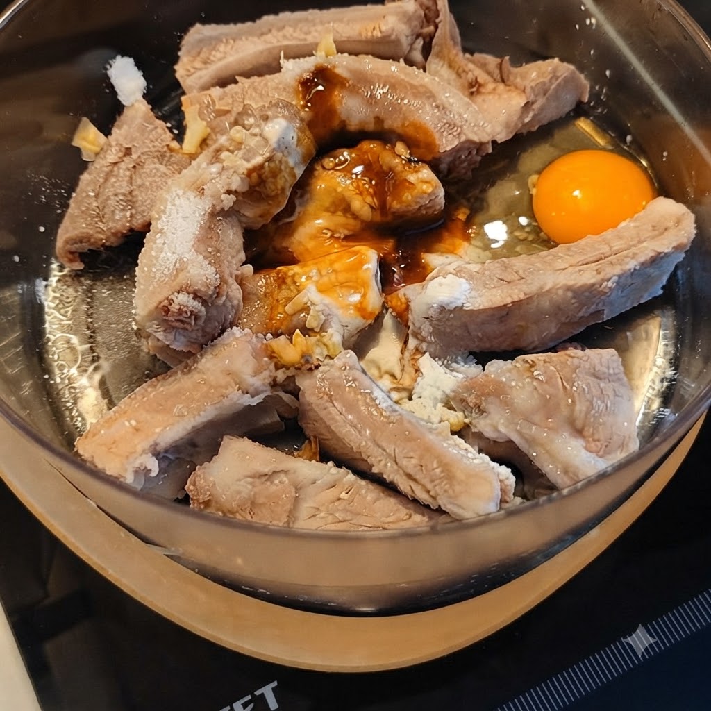 Schweinerippchen werden mit verschiedenen Soßen und einem aufgeschlagenen Ei in einer Rührschüssel mariniert.