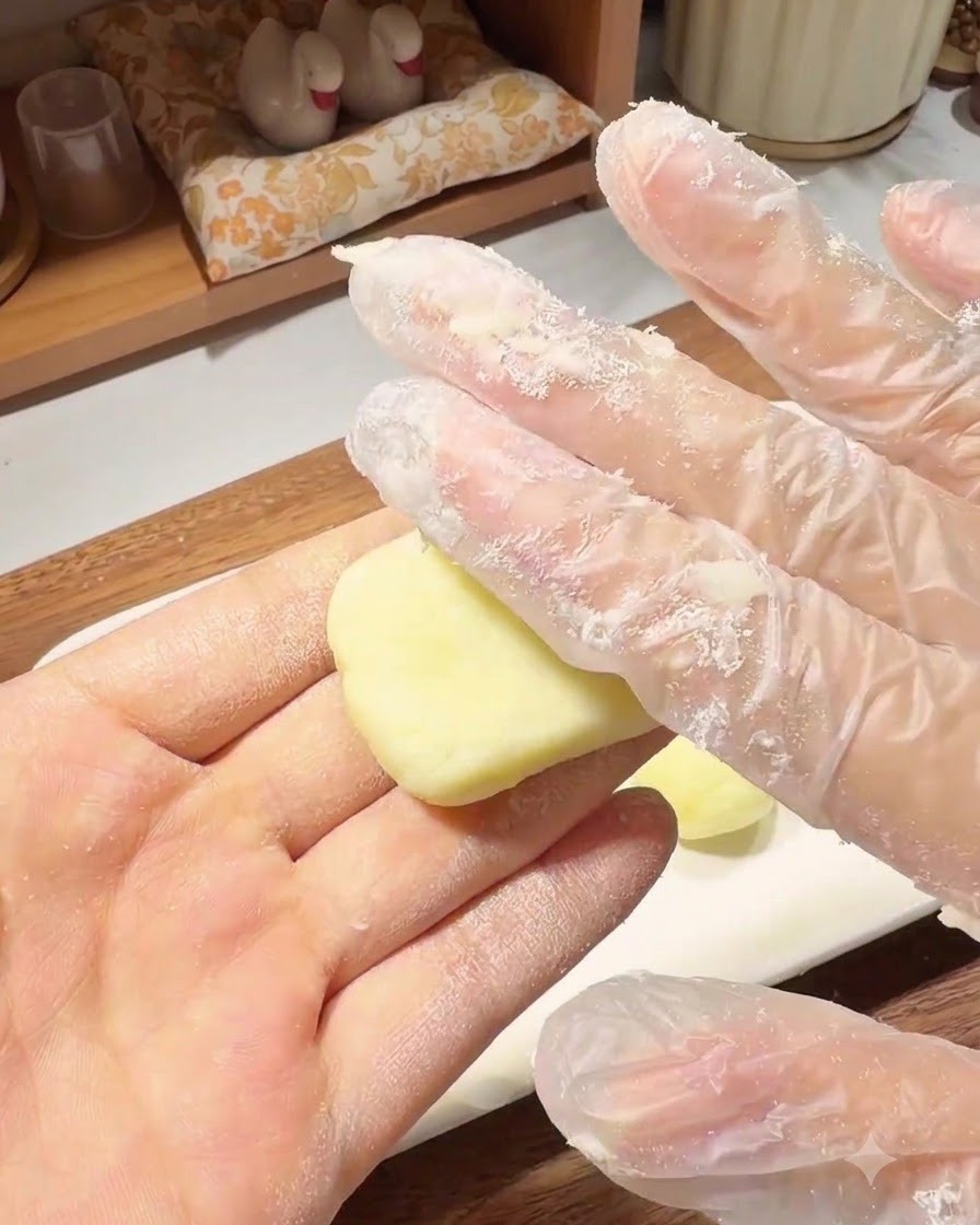 Eine behandschuhte Hand drückt eine kleine Kartoffelteigkugel in der Handfläche flach zu einem runden Puffer.