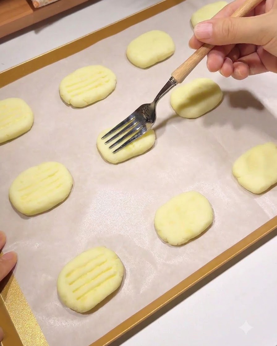 Eine Gabel mit Holzgriff drückt ein Muster aus parallelen Linien in einen geformten Kartoffelpuffer auf einem Backblech.