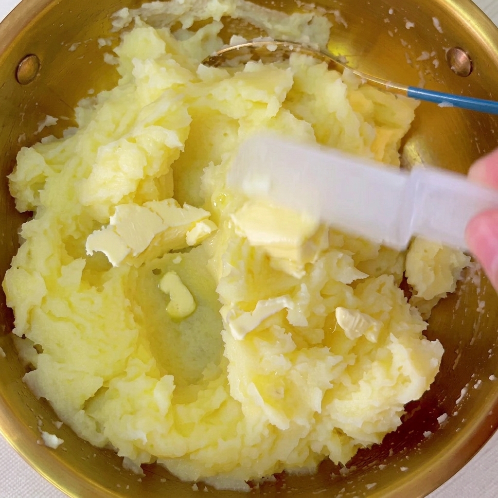 Butterstücke werden in die Schale mit dem warmen Kartoffelpüree eingearbeitet.