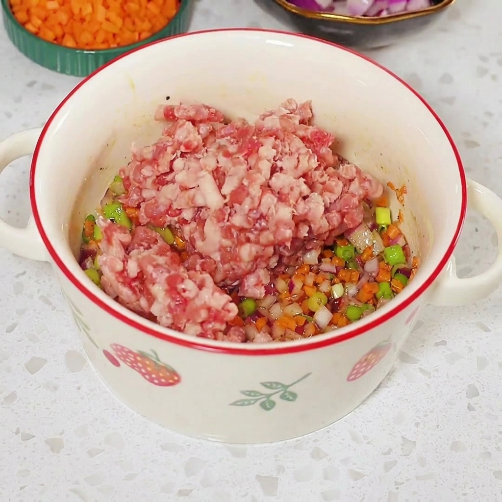 Rohes Hackfleisch auf der gewürzten Gemüsemischung in einer weißen Schüssel.