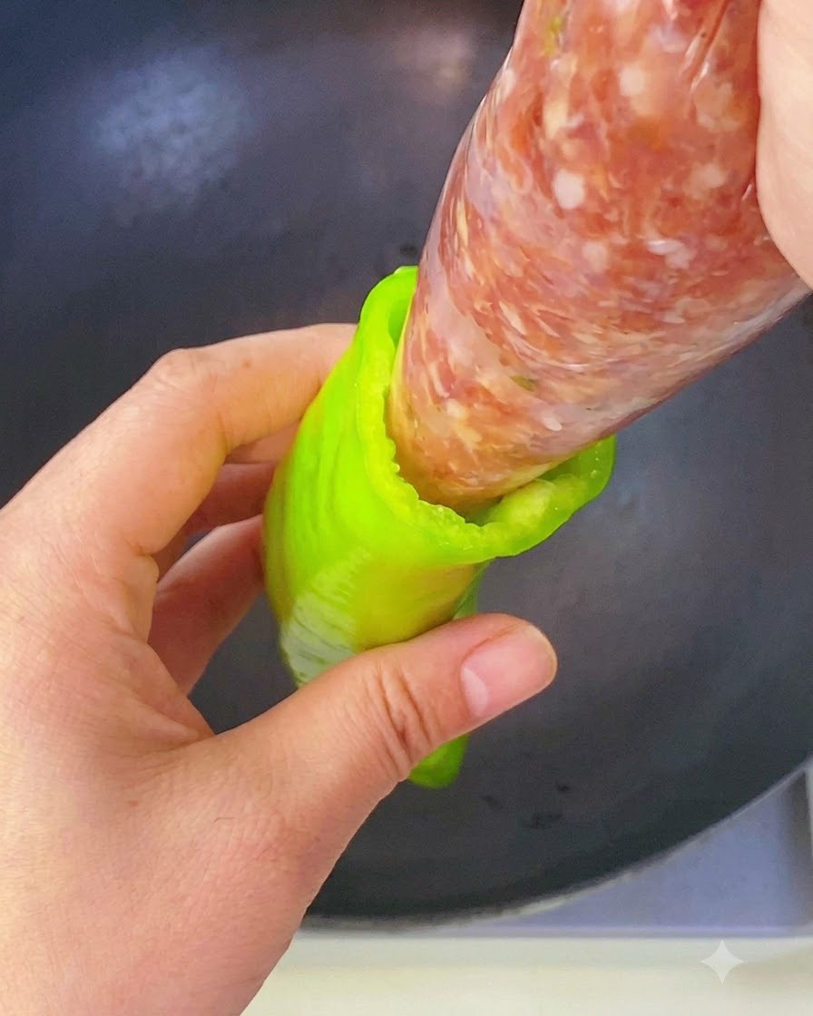 Eine Hand drückt gewürzte Fleischfüllung aus einem Spritzbeutel direkt in die Höhlung einer grünen Paprika.