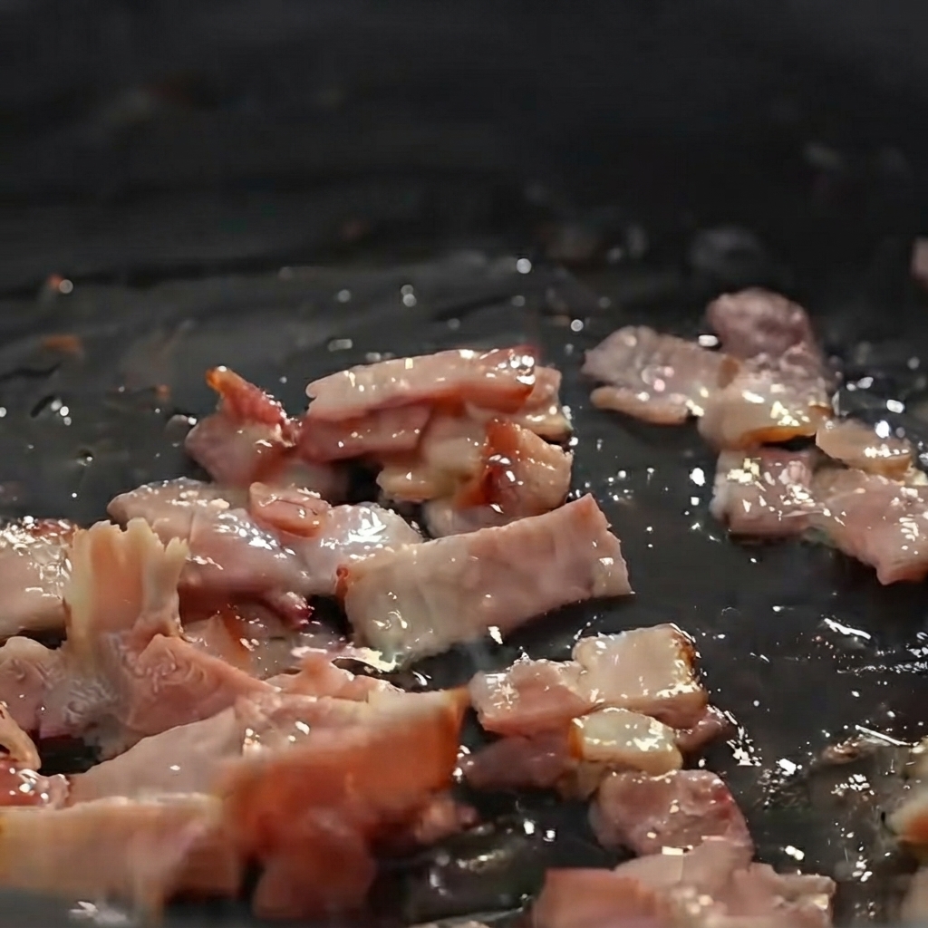 Gewürfelte Kartoffeln, Zwiebeln und Sellerie werden mit Speckstücken in einer Pfanne angebraten.