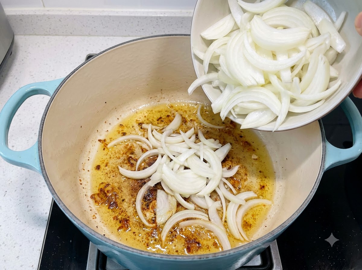 Geschnittene Zwiebeln werden aus einer kleinen Schüssel in einen Topf mit angebratenem Knoblauch und Öl gegeben.