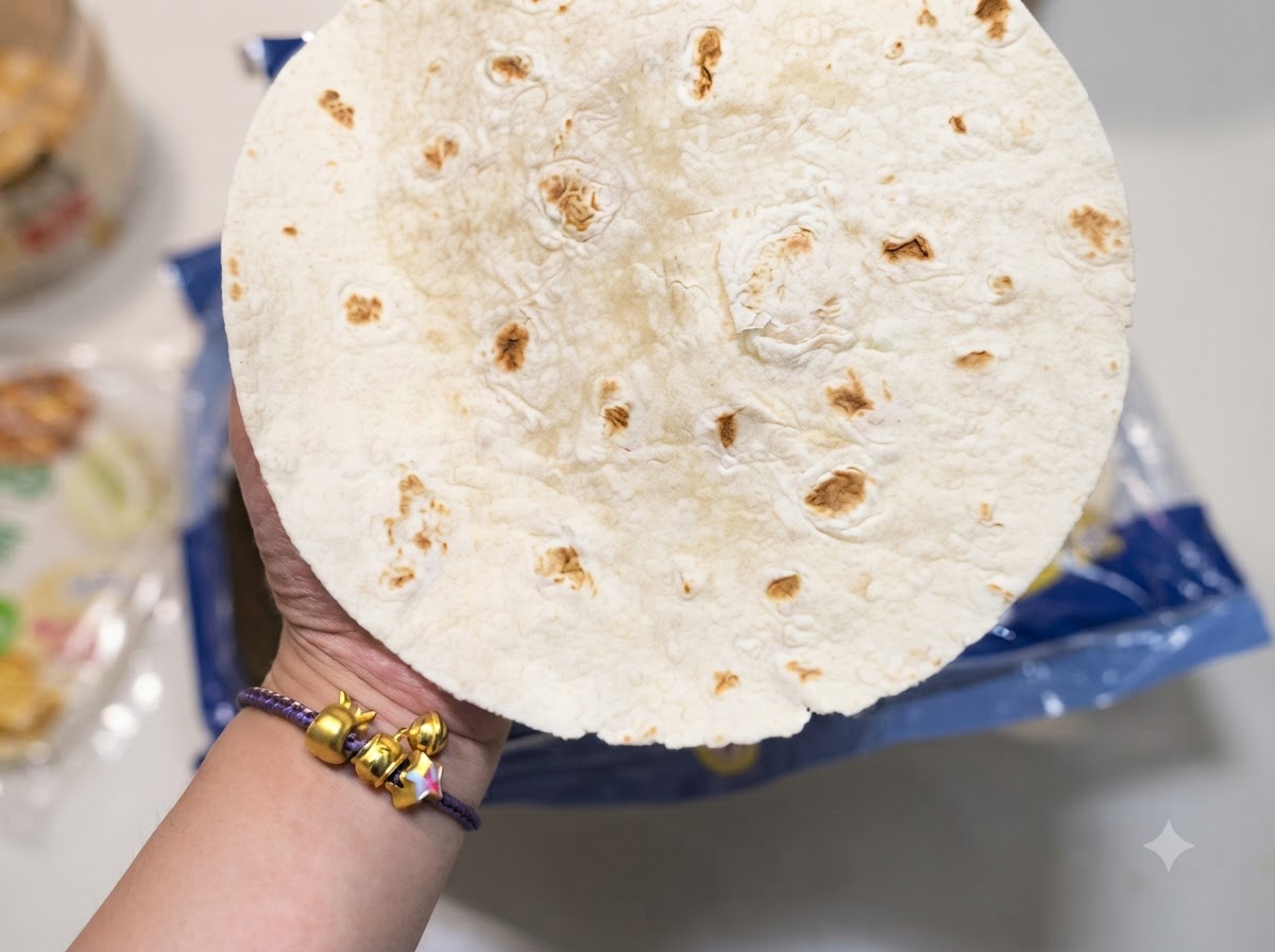 Eine Nahaufnahme einer Hand, die eine runde Mehl-Tortilla mit charakteristischen braunen Flecken hält.