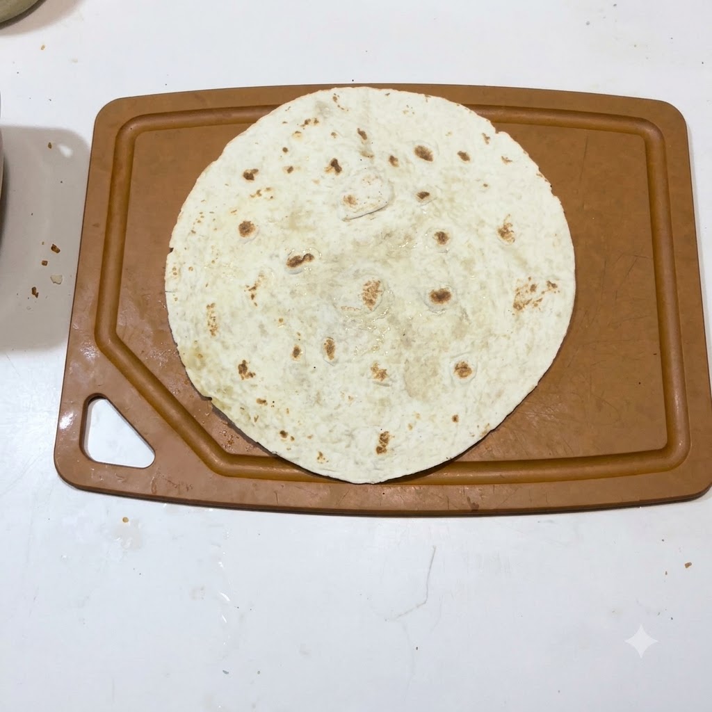 Eine einzelne warme Tortilla flach auf einer braunen Schneidebrett-Oberfläche ausgelegt.