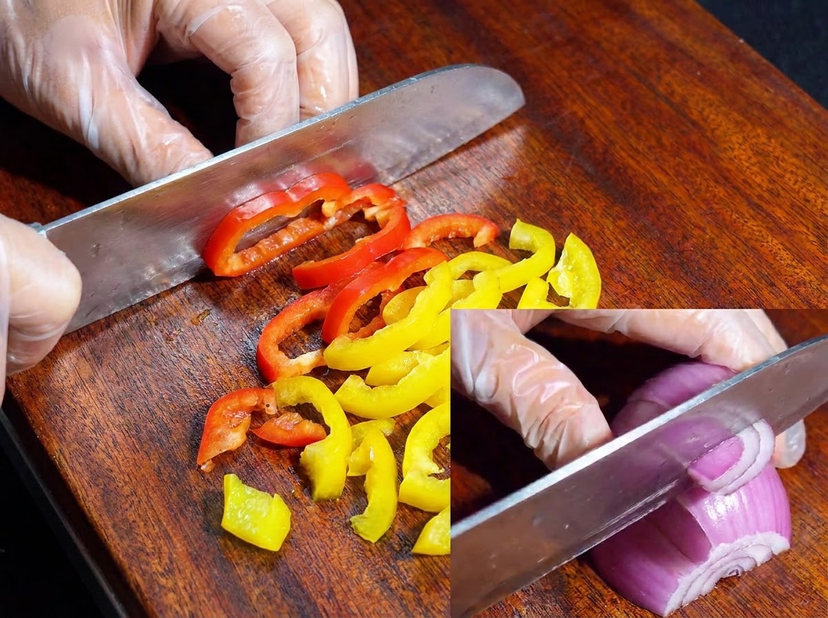 Ein Messer schneidet bunte Paprika und rote Zwiebeln auf einem Holzschneidebrett.