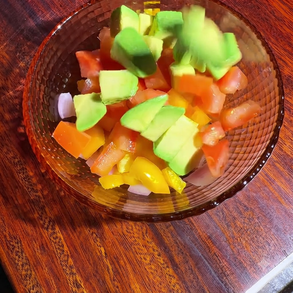 Eine Schüssel mit gewürfeltem Gemüse und Avocado, die mit Öl und Zitronensaft vermengt und gewürzt wird.