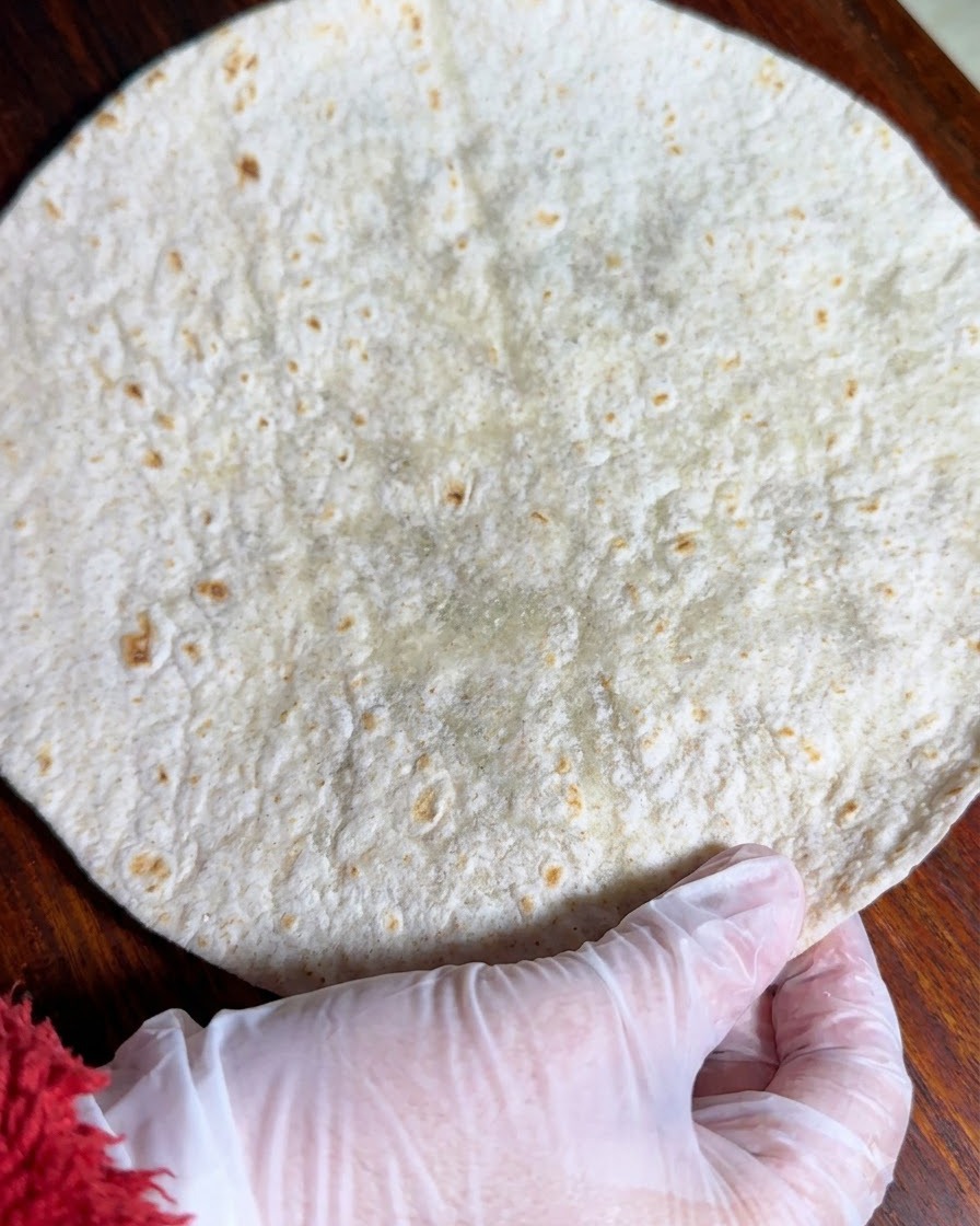 Eine Vollkorntortilla liegt flach auf einer Holzoberfläche ausgebreitet.