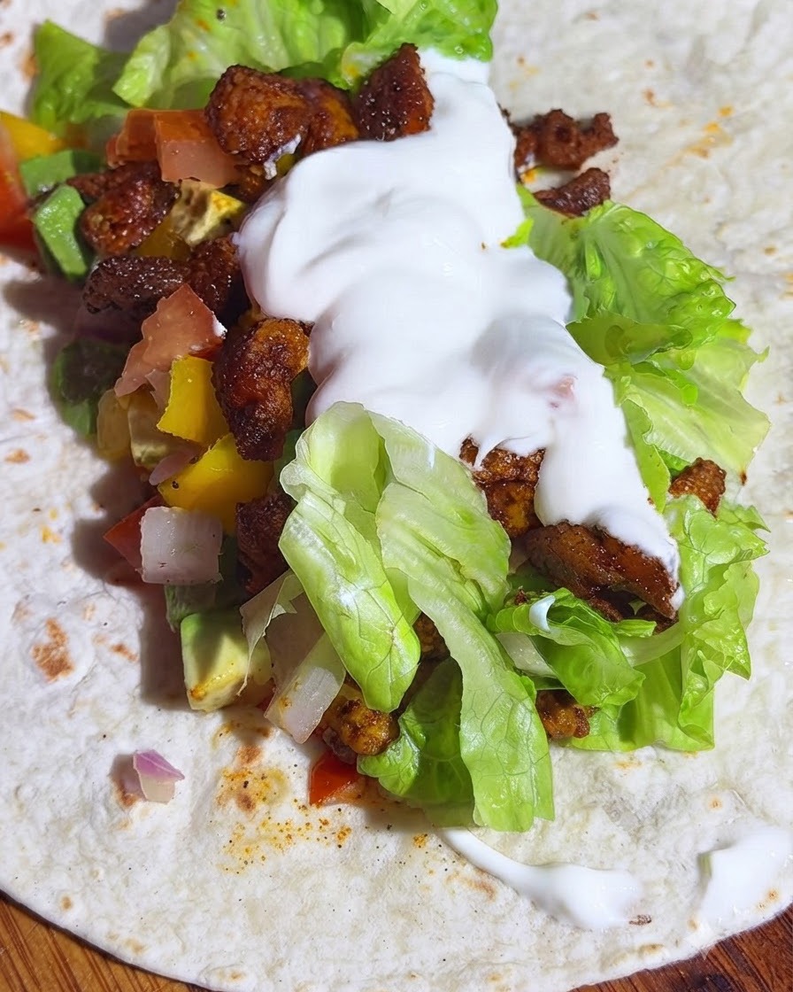 Eine Vollkorntortilla belegt mit Salat, Avocadosalsa, Hähnchen und einem Klecks Joghurt.