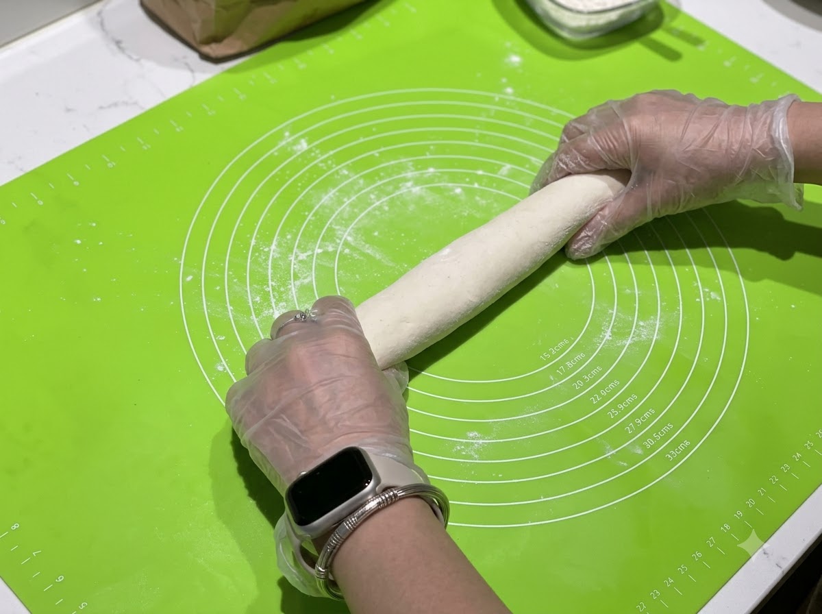 Hände rollen eine Teigrolle auf einer grünen Silikonmatte mit Messkreisen.