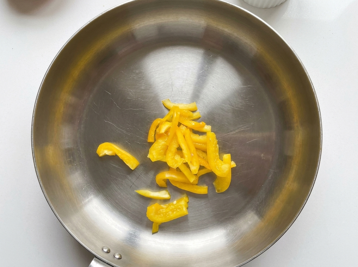 In Scheiben geschnittene gelbe Paprika in der Mitte einer Edelstahlpfanne.