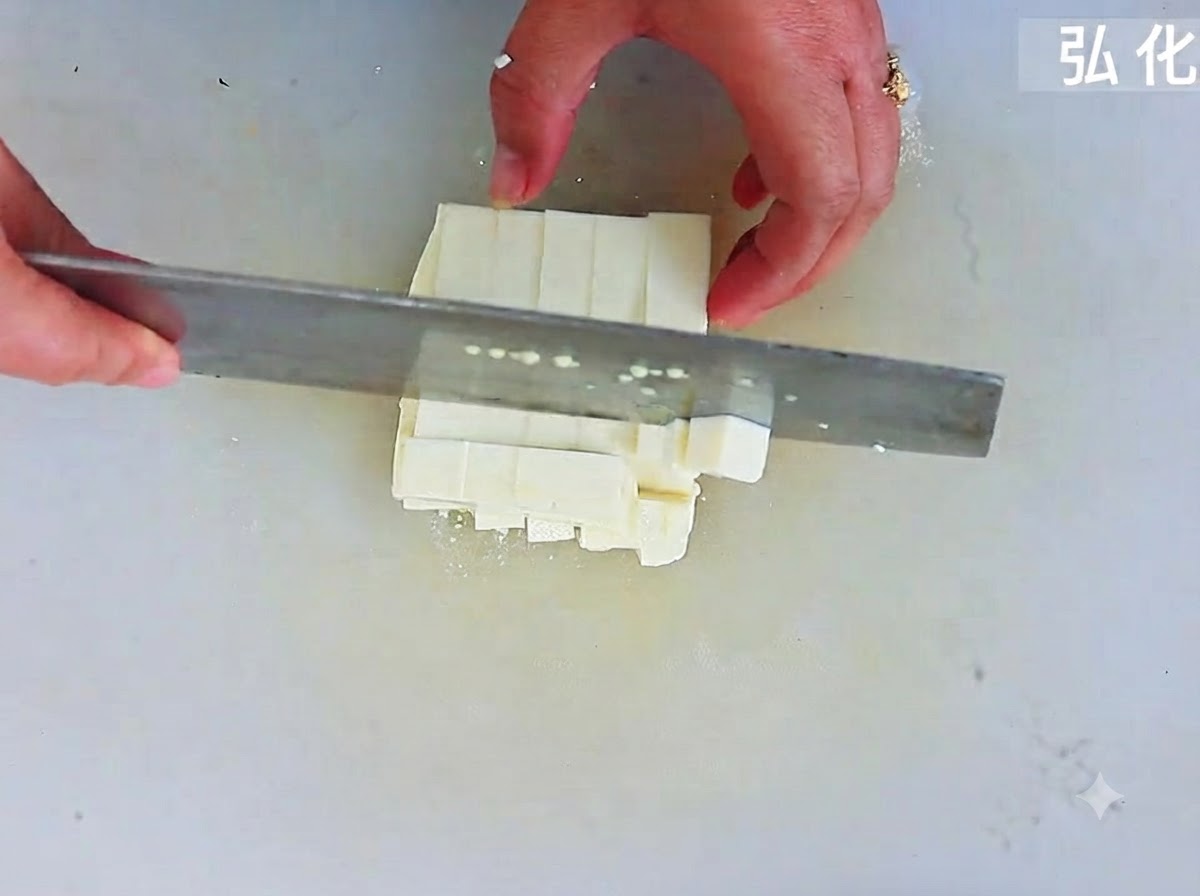 Weicher Tofu wird mit einem großen Kochmesser auf einem Schneidebrett in gleichmäßige quadratische Würfel geschnitten.