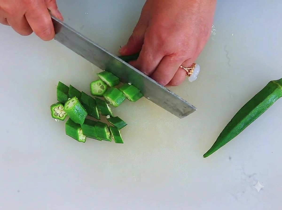 Frische grüne Okraschoten werden auf einem Schneidebrett in kleine, sternförmige Scheiben geschnitten.
