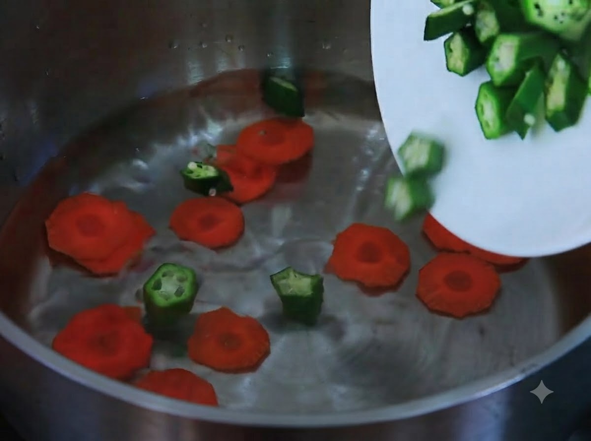 Geschnittene Karotten und gehackte Okra gleiten von einem weißen Teller in einen mit Wasser gefüllten Topf.
