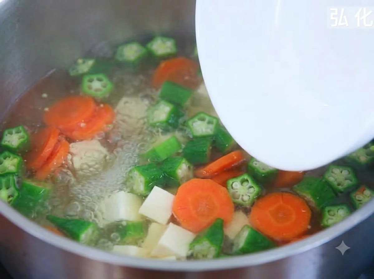 Tofuwürfel werden von einem Teller in einen köchelnden Topf mit Gemüsesuppe gegeben.