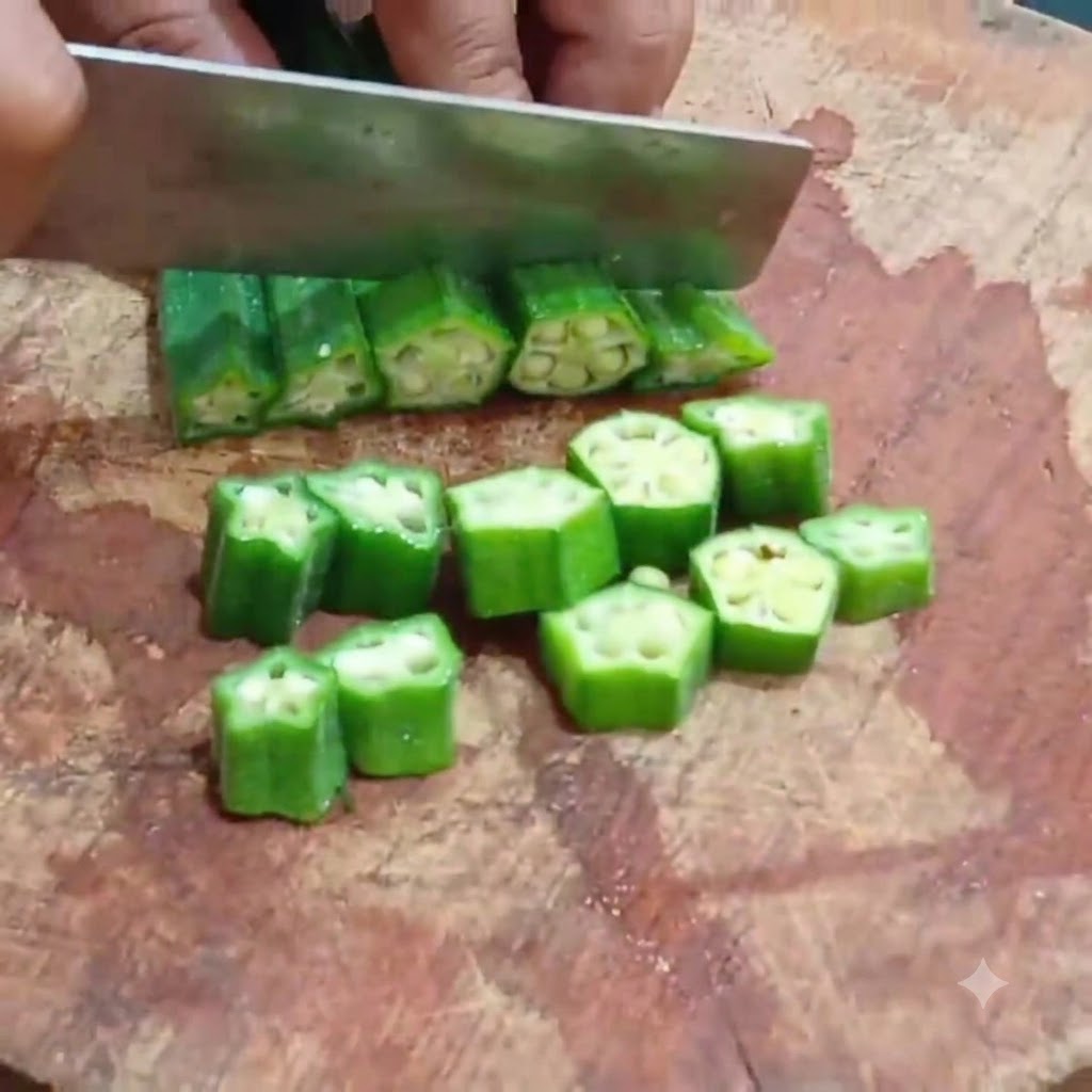 Ein Küchenmesser schneidet blanchierte Okra auf einem Holzschneidebrett in gleichmäßige runden Scheiben.