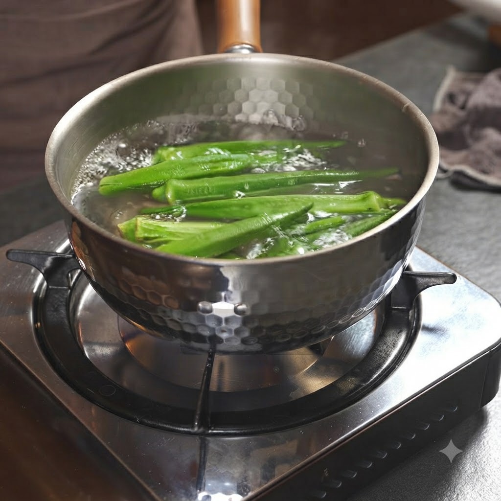Grüne Okraschoten kochen in einem Metalltopf voller Wasser auf einem Herd.