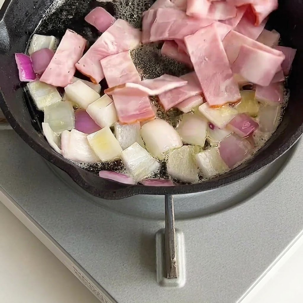 Speckstücke werden mit Zwiebeln in der Pfanne vermischt und angebraten.