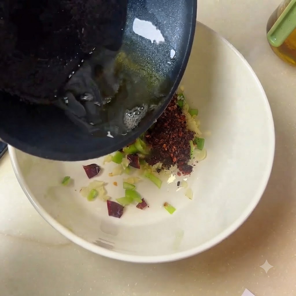 Heißes Öl strömt aus einer Pfanne in eine weiße Schüssel gefüllt mit Gewürzen und Aromen.