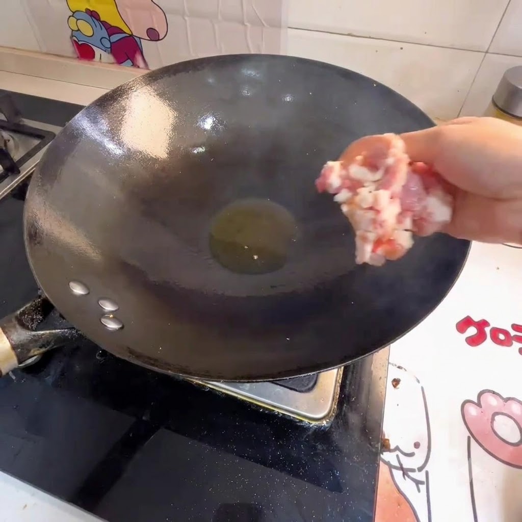 Eine Hand gibt Hackfleisch in einen Wok mit heißem Öl.