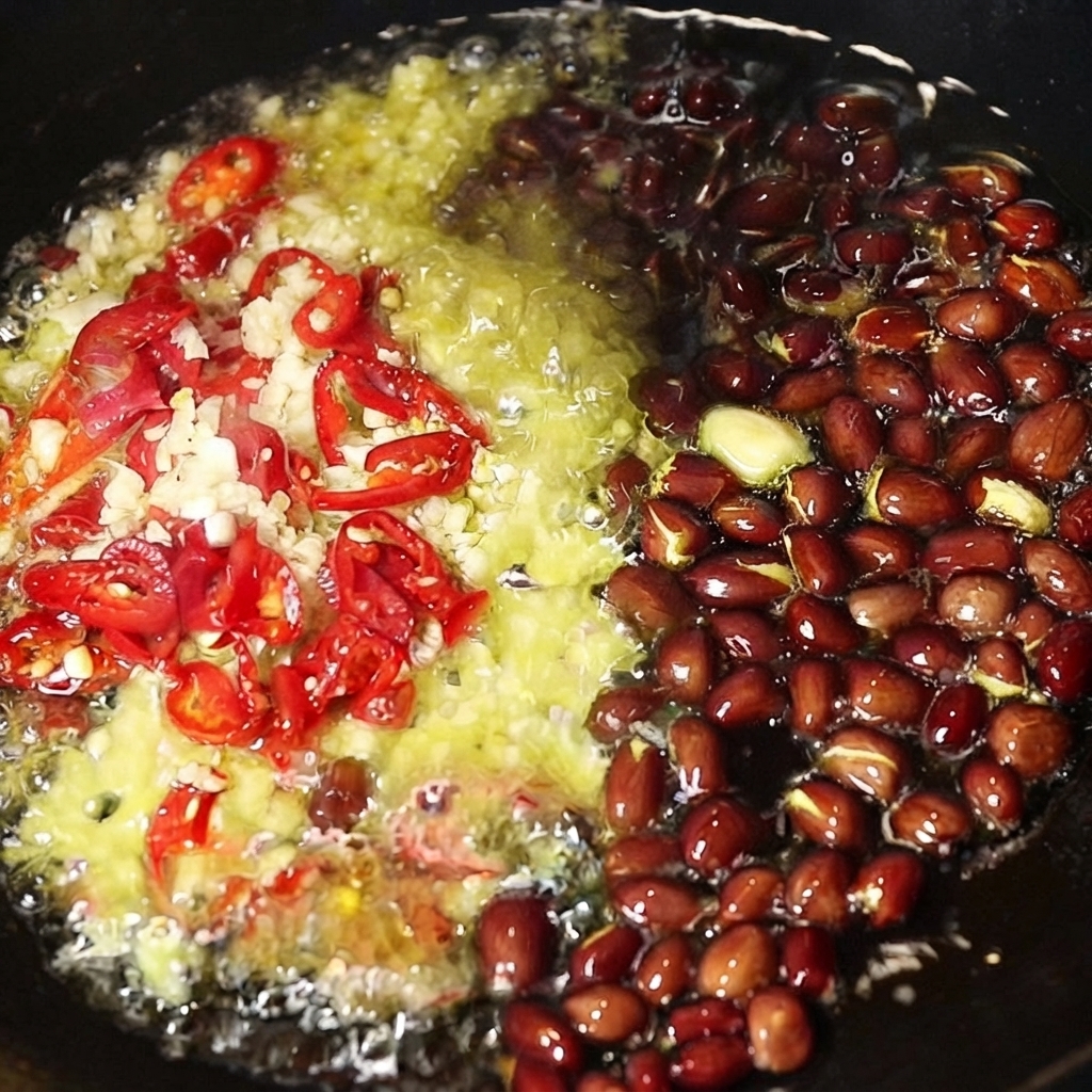 Gehackter Knoblauch, in Scheiben geschnittene rote Chilis und ganze Erdnüsse brutzeln in heißem Öl in einem Wok.