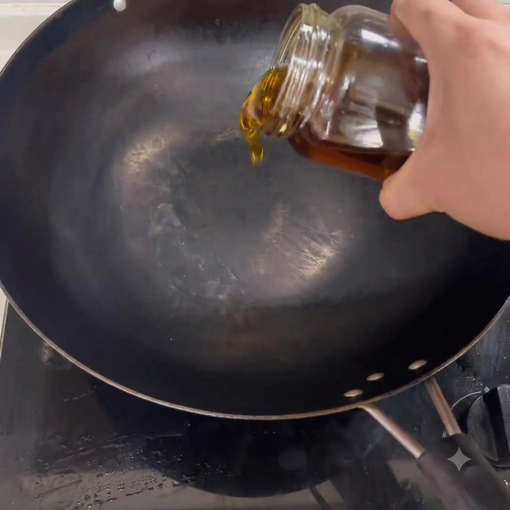 Kochöl fließt aus einem Glas in einen schwarzen Wok, der auf einem Herd steht.