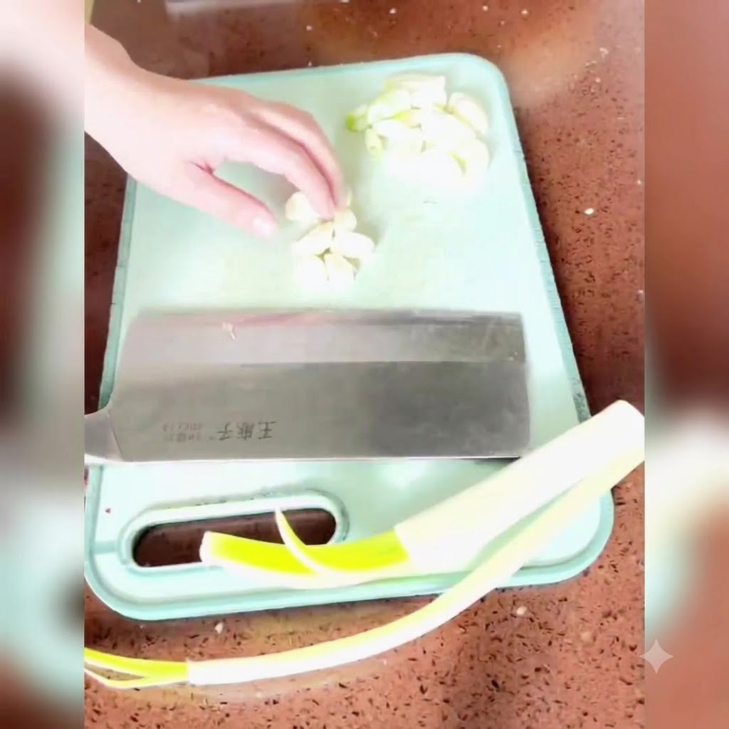 Frühlingszwiebeln, Ingwer und Knoblauch werden auf einem grünen Schneidebrett mit einem großen Beil gehackt.