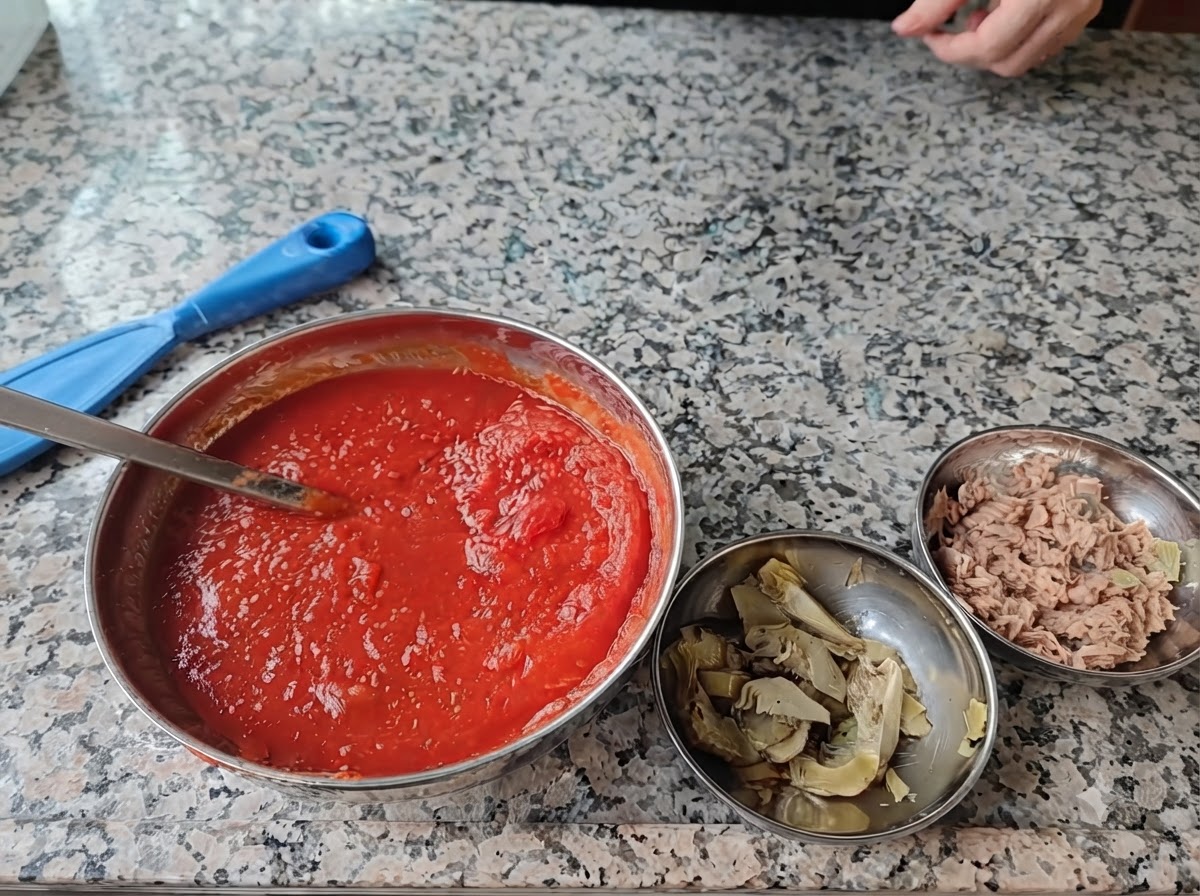 Vier Edelstahlschüsseln mit Pizzazutaten auf einer Marmorfläche.